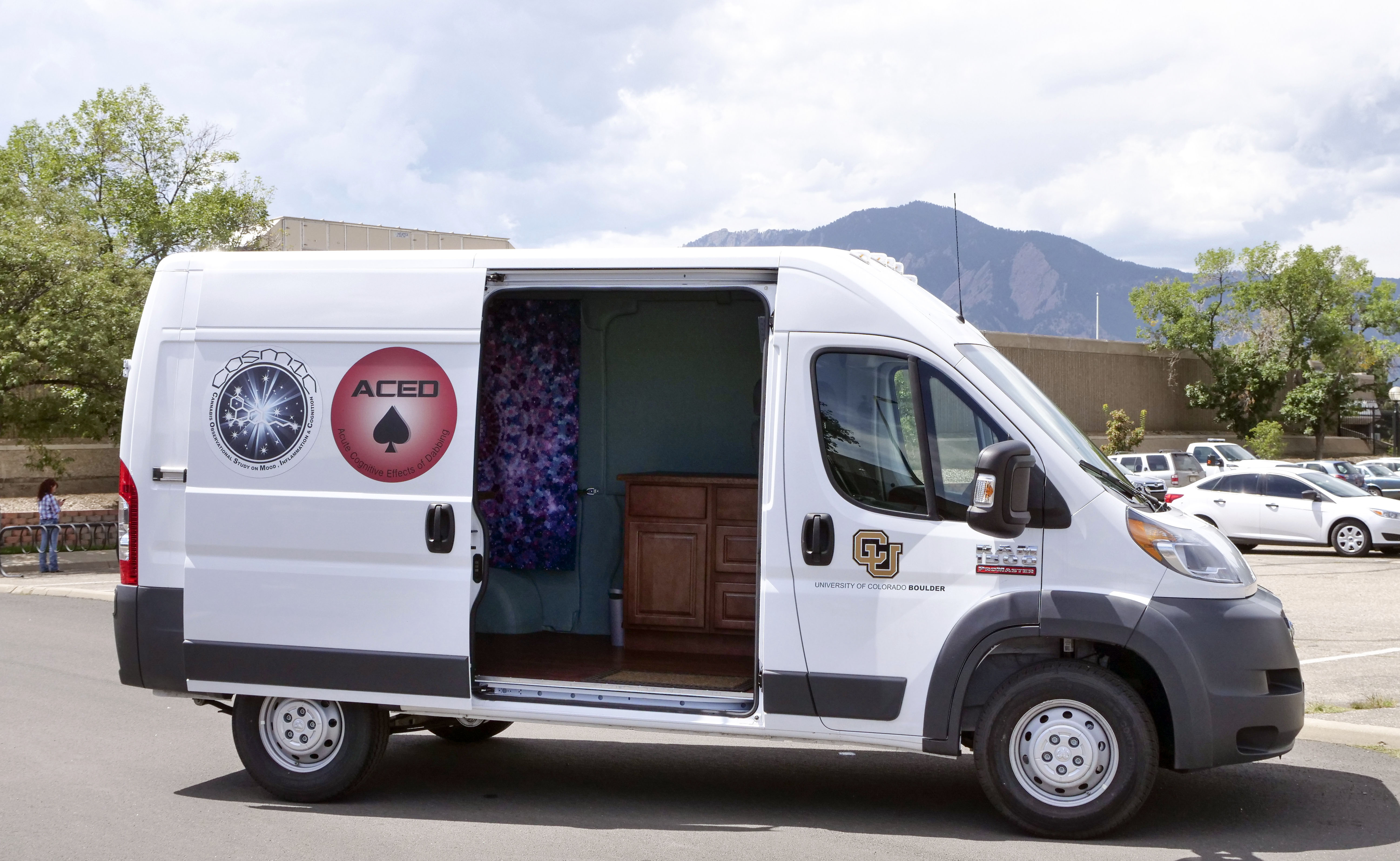 A white van with its sliding door open, parked in a lot, with mountains in the background. Decals on the side refer to scientific studies.