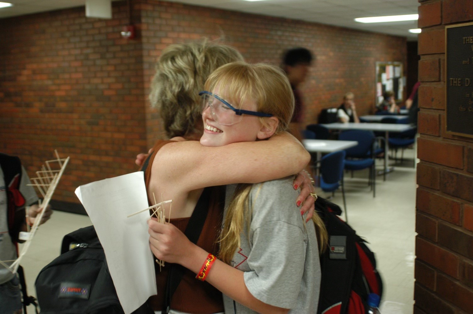 In a photo from high school, Christine McGinn hugs her mother in a school hallway, clutching a handful of balsa wood sticks.  