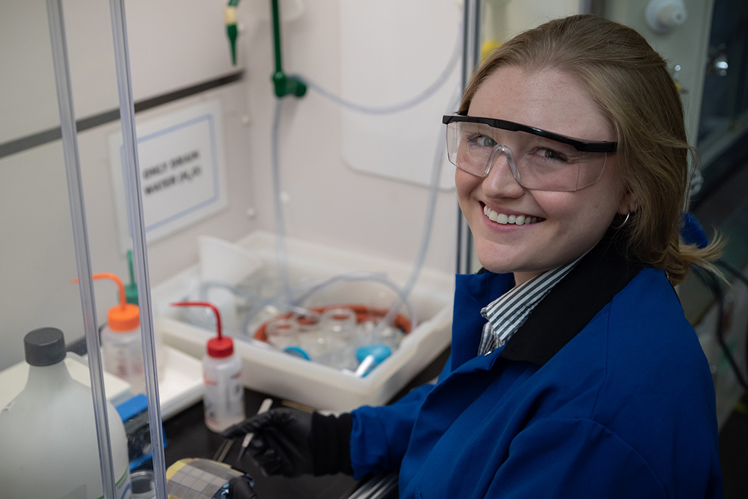 Christine McGinn wears safety glasses as she handles plastic bottles and other materials in the lab. 