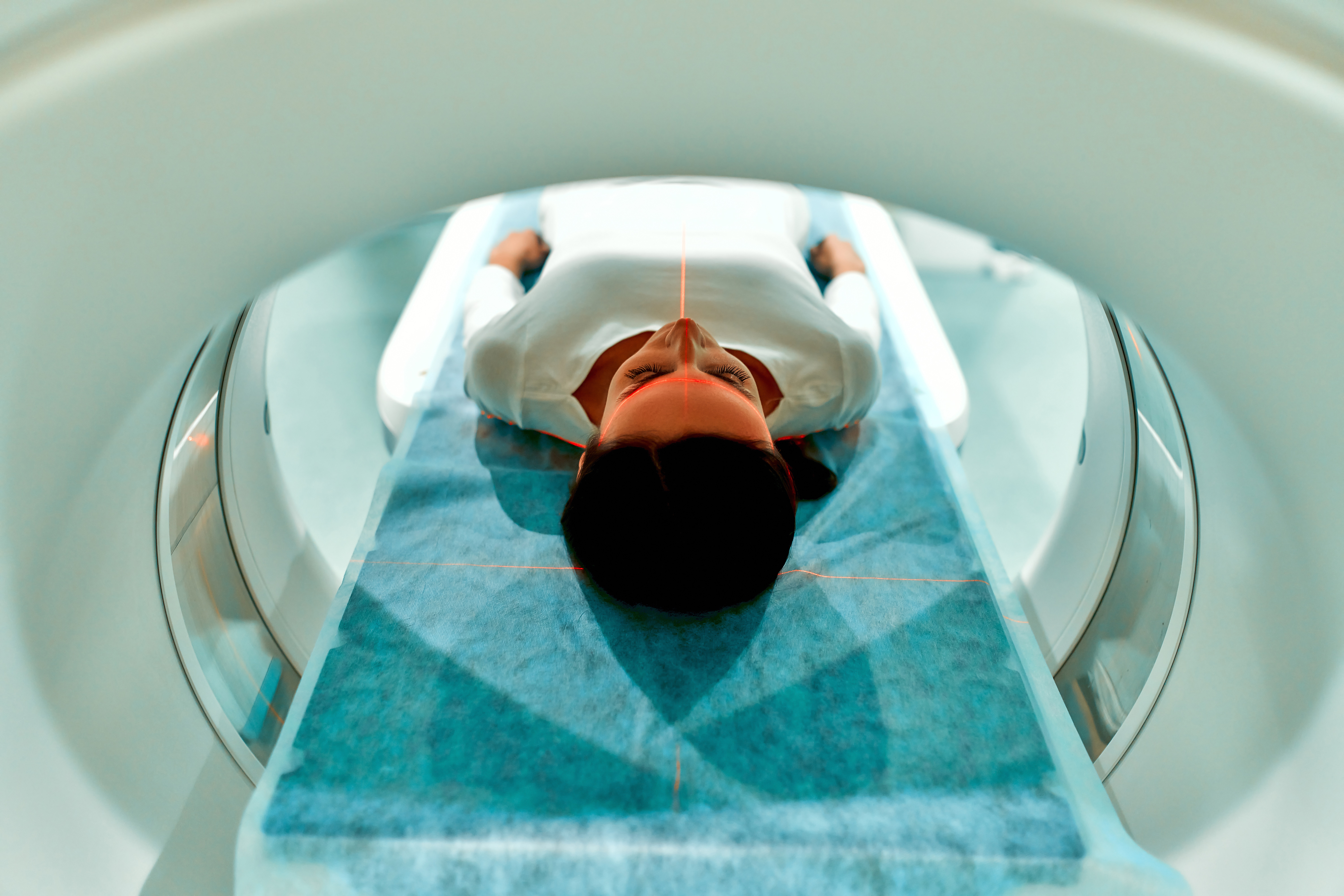 View through the top end of an MRI machine as a dark-haired patient lies inside. 