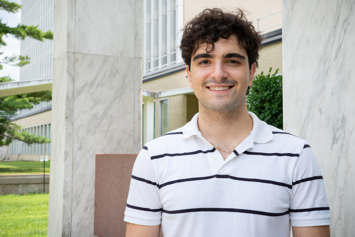 Navid Misaghian stands smiling outside a large building on the NIST campus. 