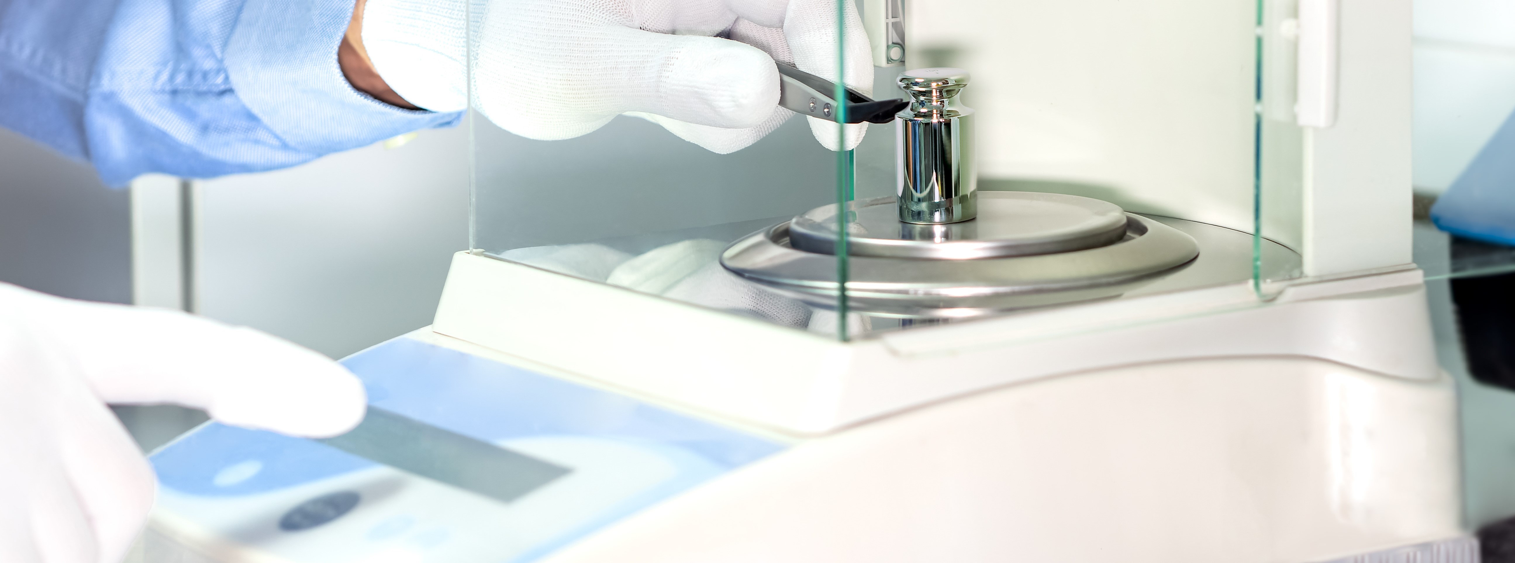 A operators hand is holding steel calibration weight to place on the analytical balance