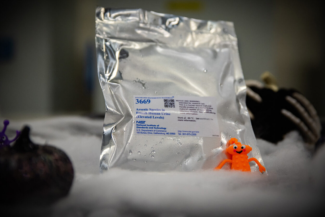 A metallic envelope with a NIST label and condensation is nestled alongside decorative Halloween pumpkins. 