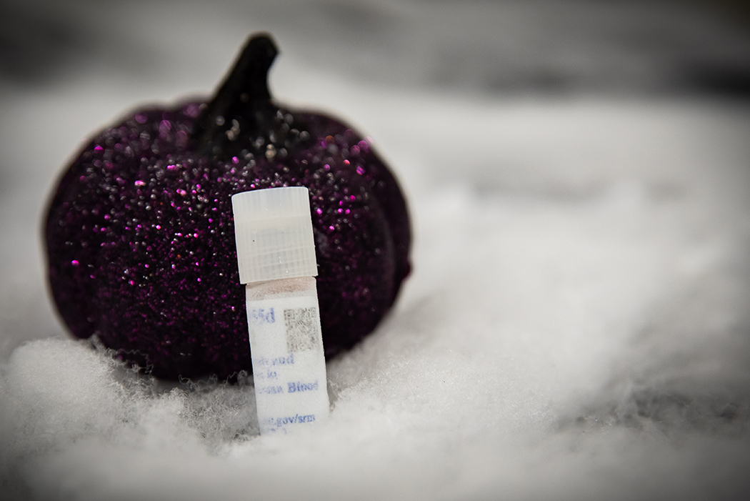 A small plastic vial covered with frost leans against a sparkly purple pumpkin decoration.