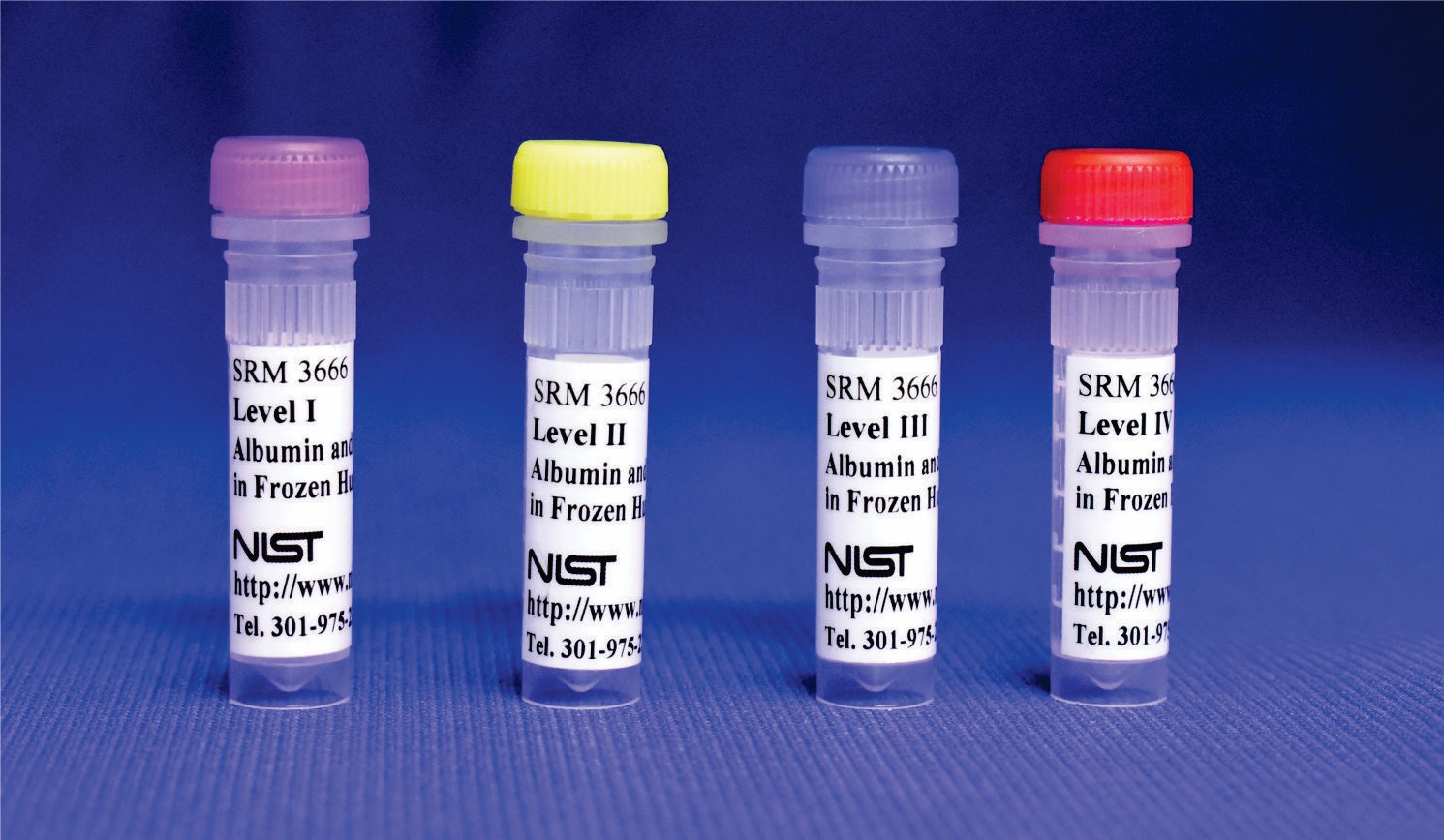 Four plastic vials with different colored lids are displayed standing up, with labels that say SRM 3666 and NIST. 