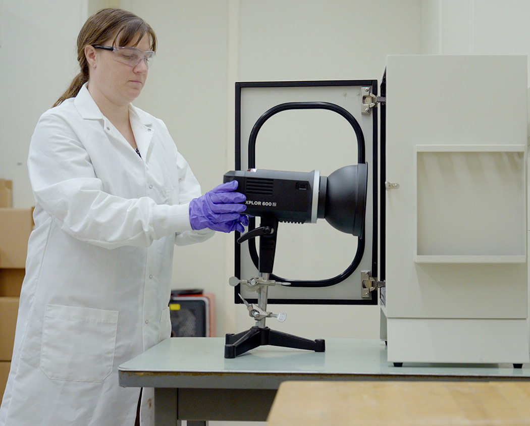 Amy Mensch, wearing a lab coat and gloves, adjusts a black camera-like device in the lab. 