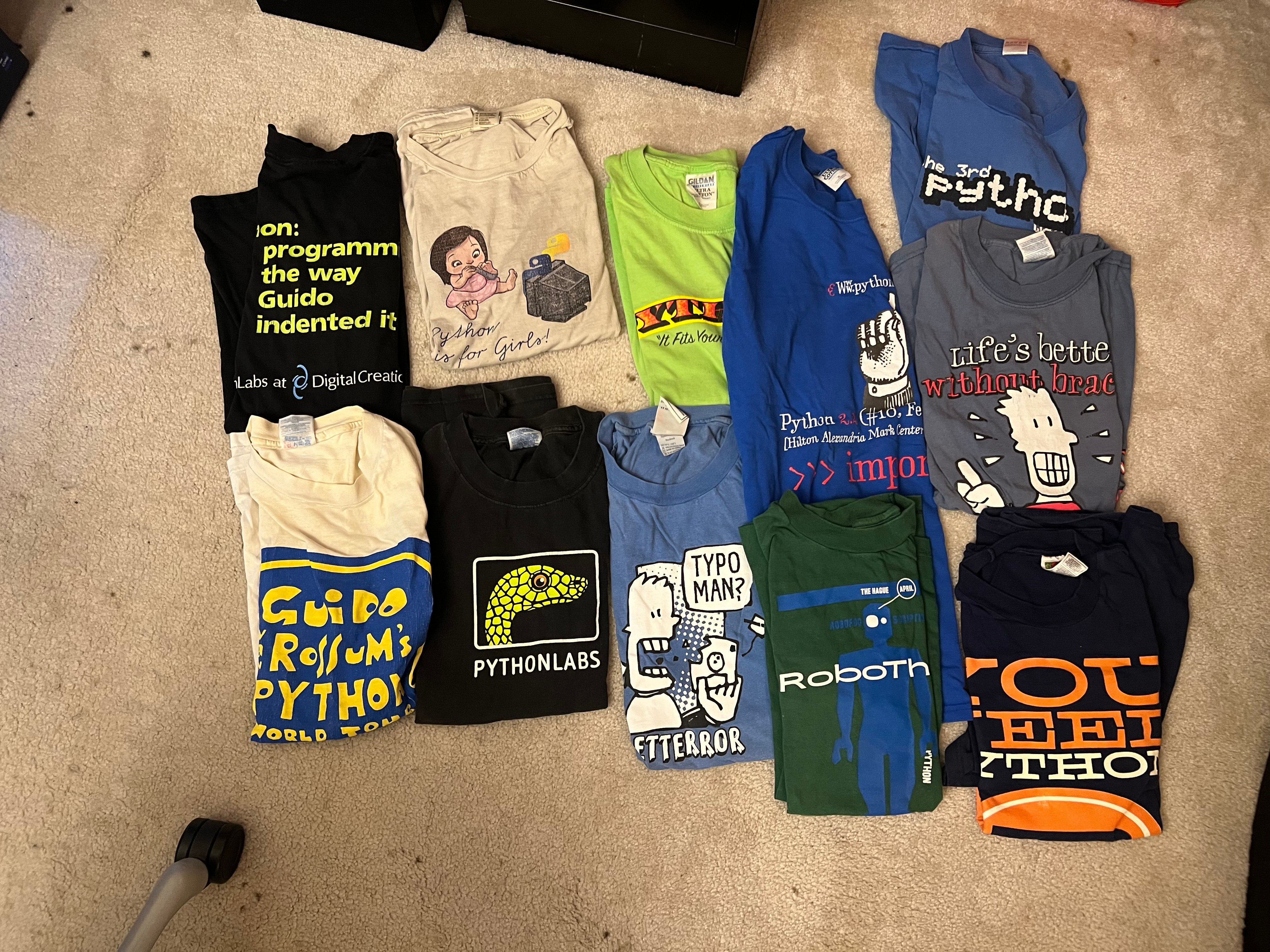 A collection of vintage computer programming T-shirts is displayed folded on the floor.