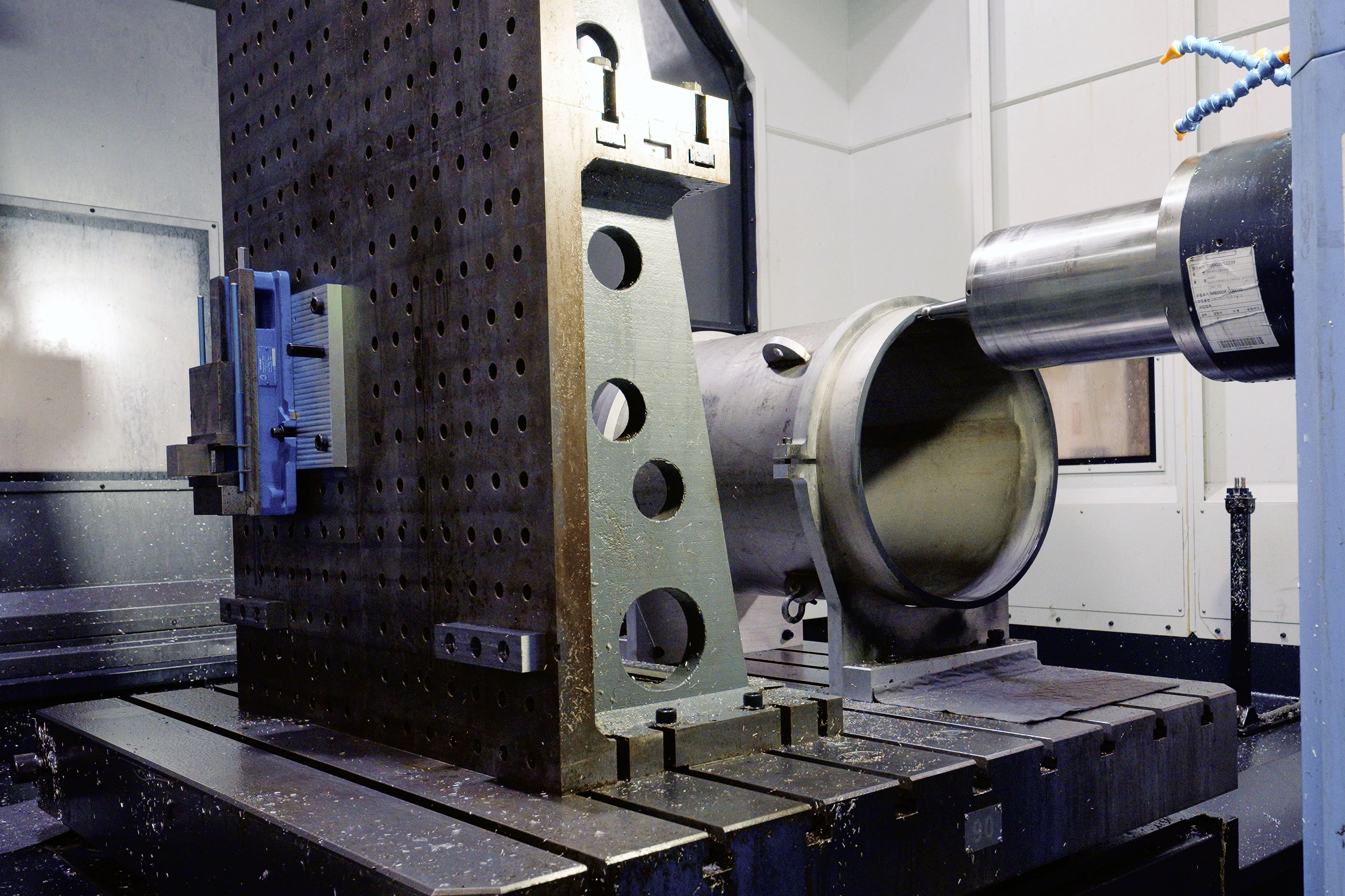 A cylinder of thick metal lies horizontally on a large support structure inside a workshop.