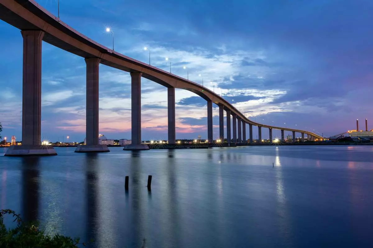 View from below of a high, long bridge on concrete supports against a darkening sky.