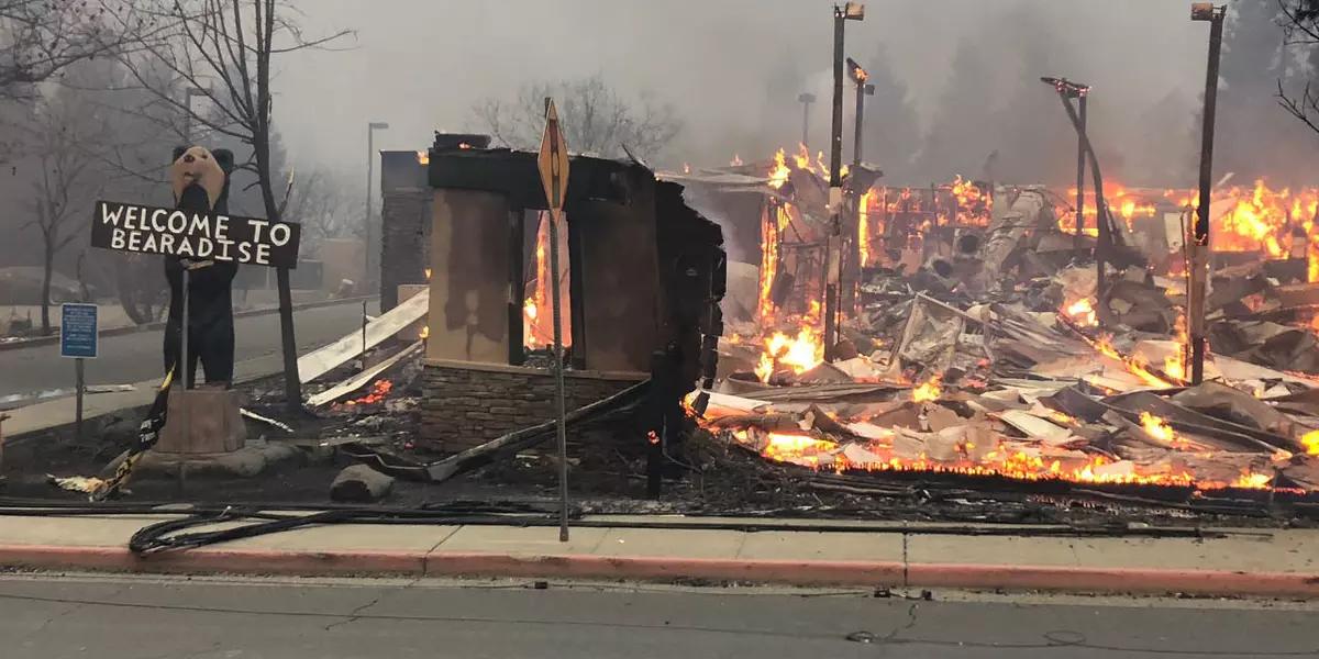 Welcome sign stands next to a burning building.