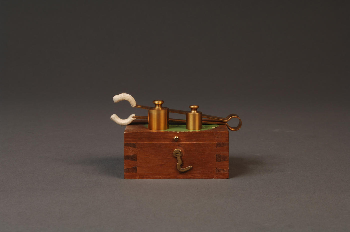 Two gold-plated brass weights sitting on top of a wood box, in front of tongs used to handle them