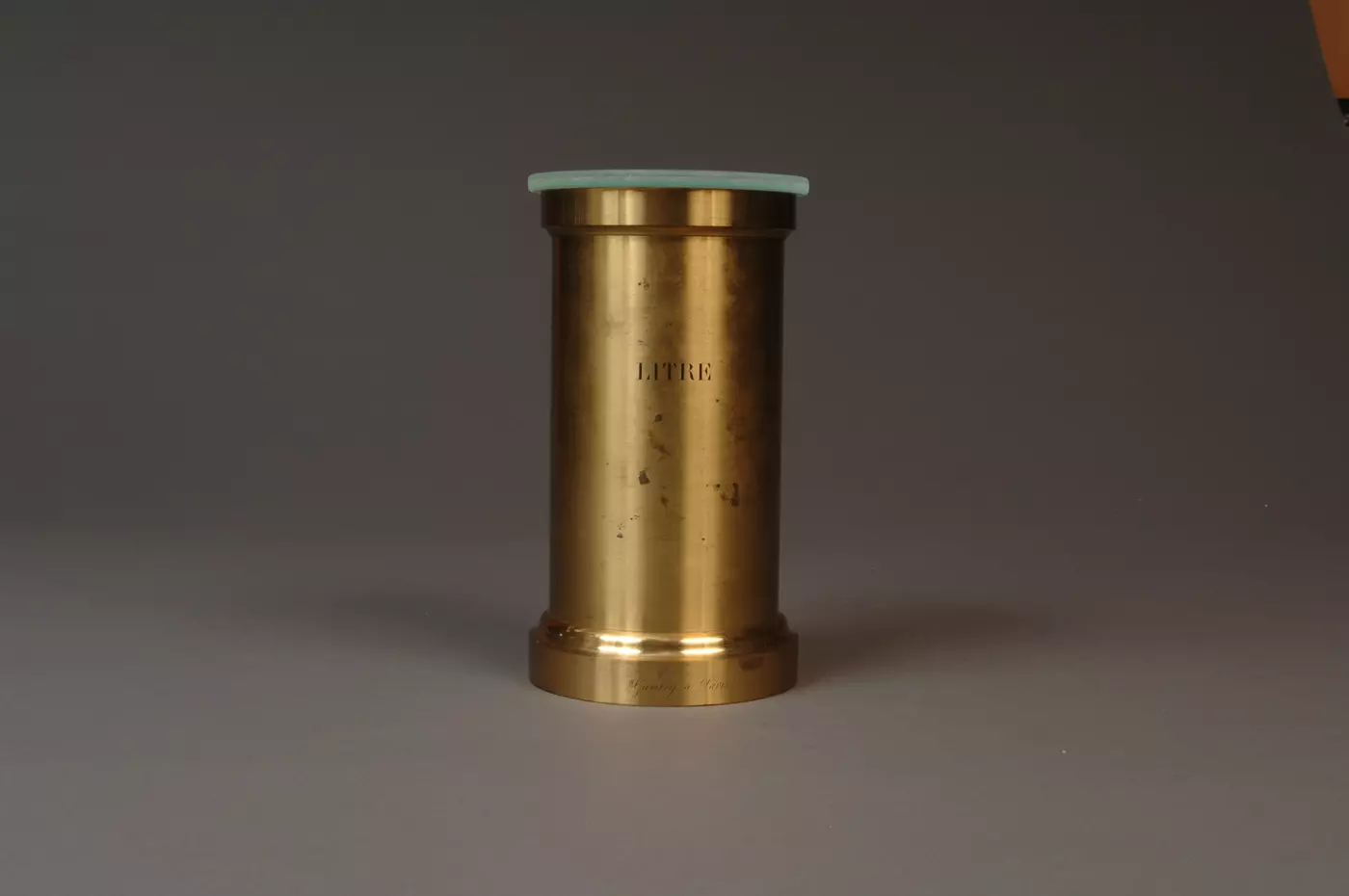 Brass volumetric standard that says "litre" on front, with glass cover on the top
