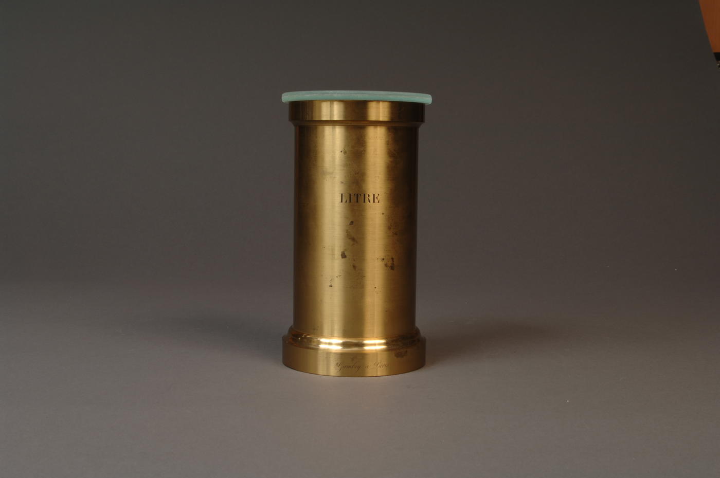 Brass volumetric standard that says "litre" on front, with glass cover on the top