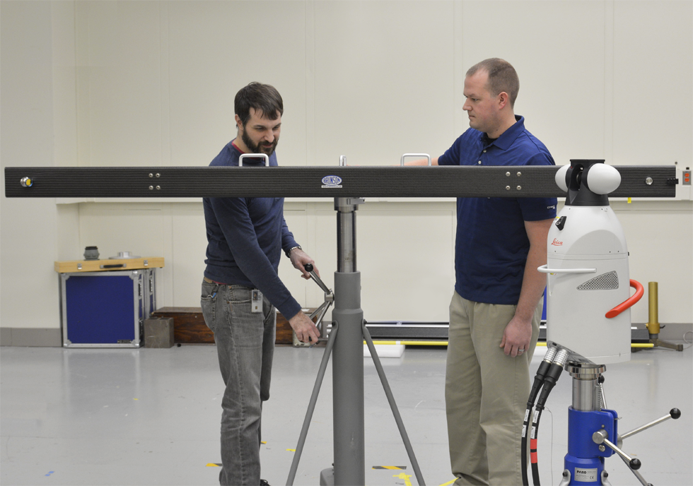 Two men stand behind a piece of metal on a custom tripod