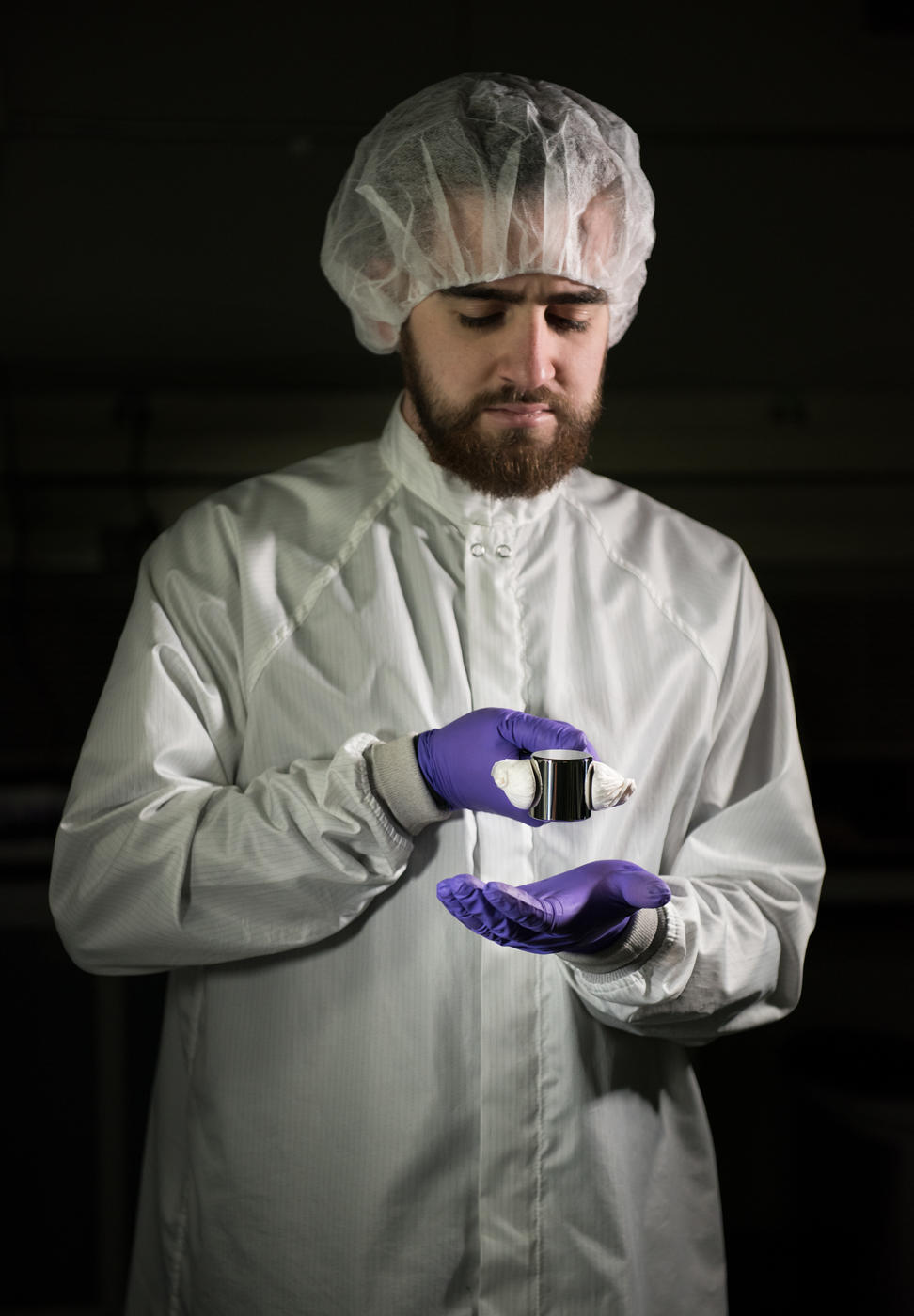 Man in clean suit and purple gloves holding a kilogram sample with tongs