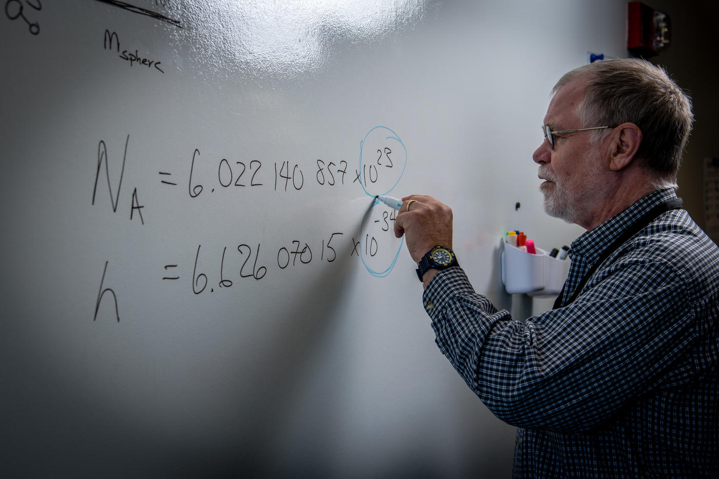 Chemist Bob Vocke stands in front of a white board writing out several complicated equations related to the mole redefinition.