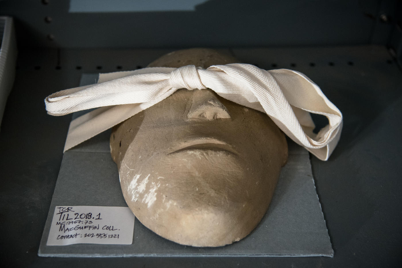 a roughly made clay mask lying face up with a piece of cloth over its eyes