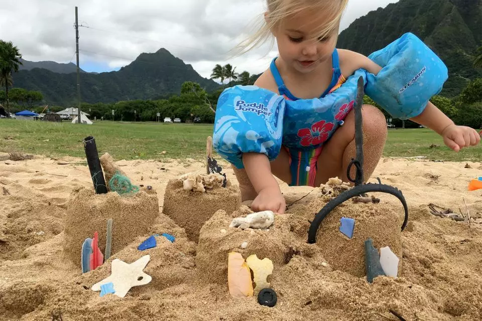 small child decorating a sandcastle with bits of plastic