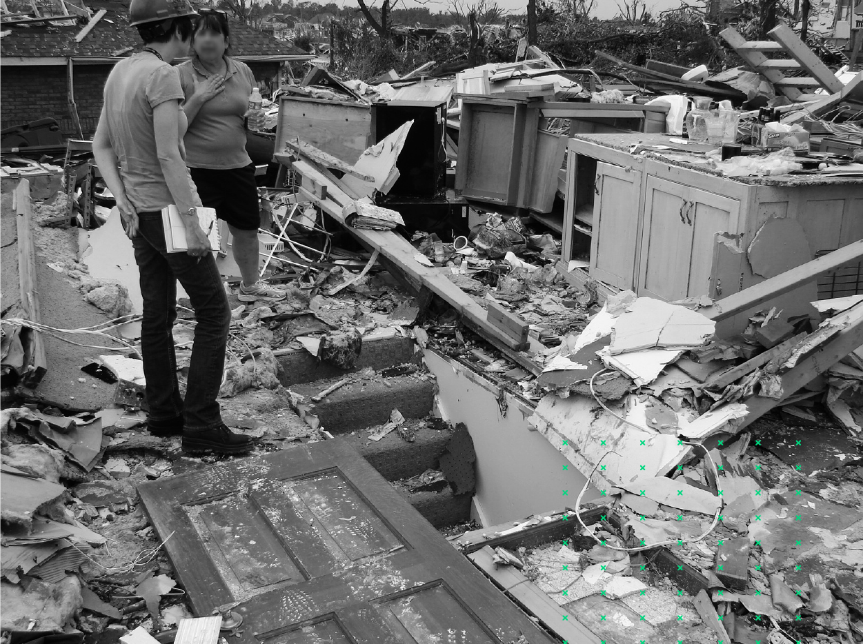 Two women stand and talk on top of a destroyed home in a black and white photo.