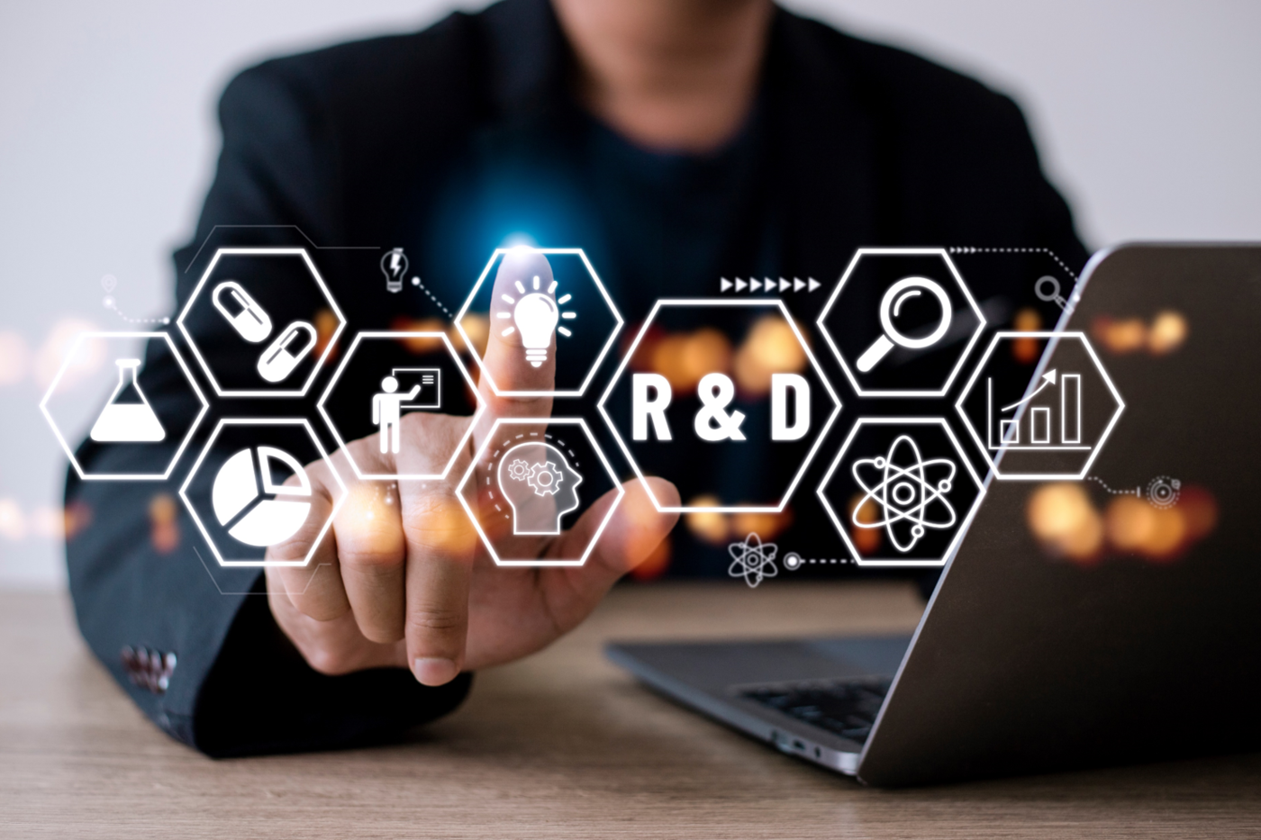 a worker, sitting at a laptop, taps a floating lightbulb icon next to the words "R&D (research and development)"