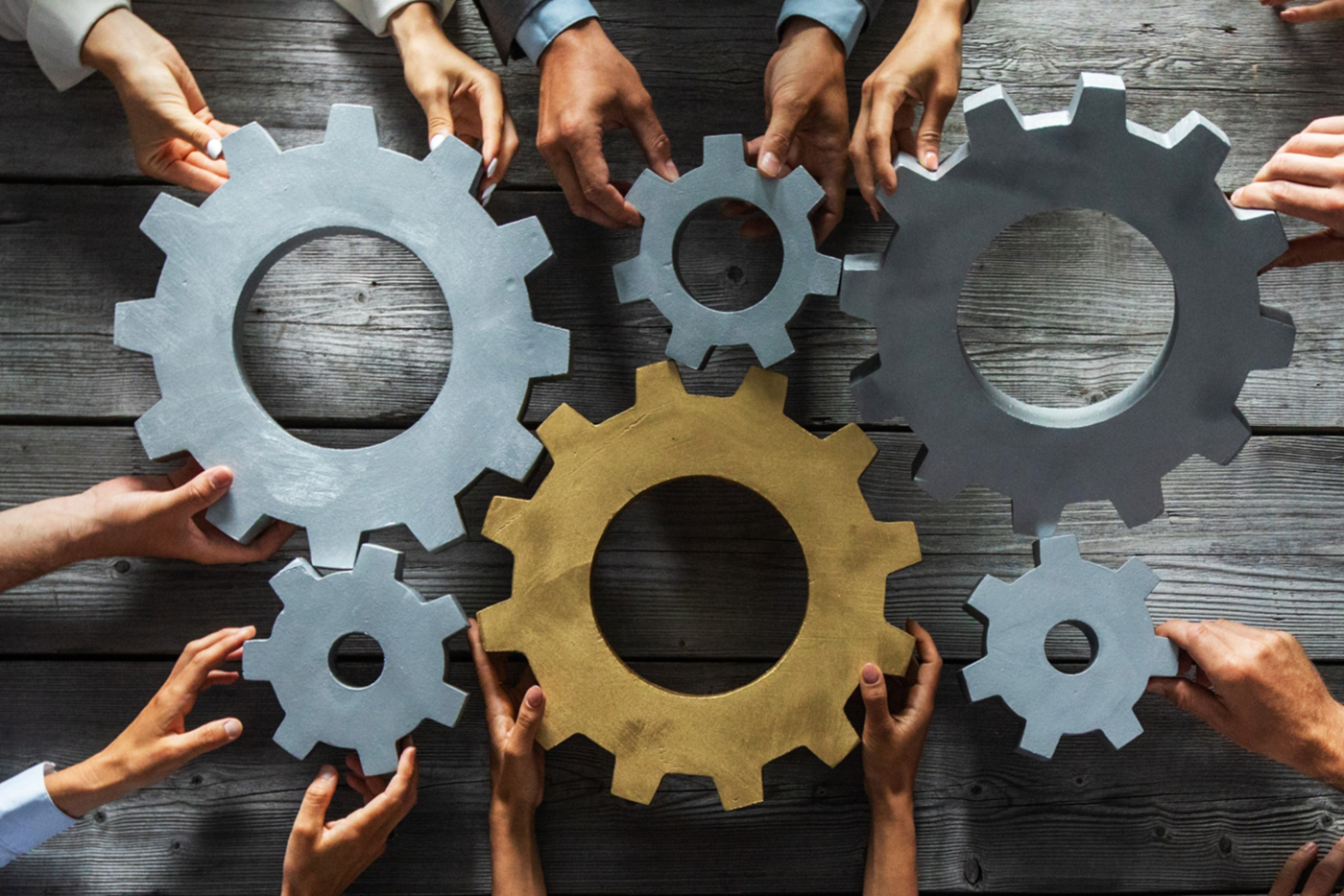 people gathered around a table push large gears together, to symbolize teamwork and collaboration