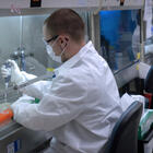 Man in white lab coat using a pipette under a hood
