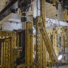 Horizontal concrete slab is visible in a forest of scaffolding and equipment in a large indoor space. 