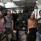 Four researchers pose standing around a large piece of scientific equipment covered with wiring and electronics. 