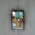 A man wearing a yellow hardhat and fire-resistant jacket points to burnt frame of a window.