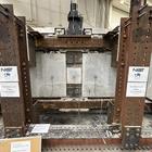 A wide view of a concrete beam assembly inside a large metal frame. A hydraulic arm is part of the metal frame, and it’s posed to press down at a section in the middle where the concrete pieces connect.