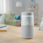 A cylindrical smart speaker sits on a wooden table in a living room. 