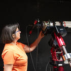 Susana Deustua looks at a large, red telescope located in a dark room. 