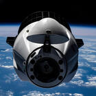 A rounded spacecraft floats in space with the blue surface of the Earth in the background.