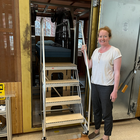 Woman poses smiling next to a set of portable stairs that lead up to a platform for an experimental MRI setup. 