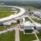 An arial view shows part of the huge enclosed loop of an accelerator, with attached buildings and parking lots.