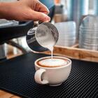 A barista pours steamed milk into a cup of espresso.