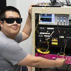 Yicheng Shi wears dark safety glasses as he poses next to a rack of electronics equipment.