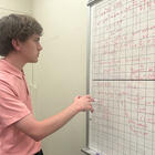 Henry Nonnemaker stands holding a marker, looking at a gridded whiteboard covered with mathematical formulas.