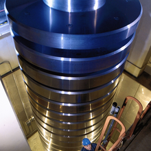 Pile several stories high of metal round cylinders with man climbing ladder alongside.