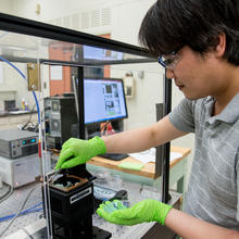 NIST postdoc Nam Nguyen inserts a silicon wafer coated with a “library” of many thousands of different thin-film thermochromic compositions into a custom-built apparatus for testing. 