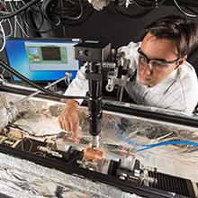 NIST's Zeehan Ahmed positions an optical fiber above a small photonic sensor inside an optical probe station