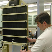 Guest researcher John Jendzurski prepares the NIST electromagnetic phantom for passage through the walk-through metal detector behind it.