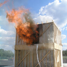 Flames coming out of the first doorway of a test structure after the floor has collapsed into the basement.