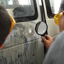 Law enforcement officers locating latent fingerprints on the side of a van.