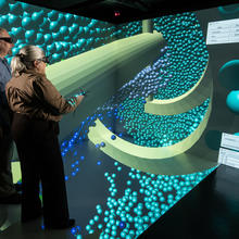 Photo of 2 researchers wearing visualization eyewear, standing in an immersive display which shows concrete particles.