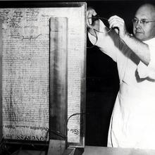 A NIST scientist stands before the Declaration of Independence, which is upright in glass, and works on the encasement