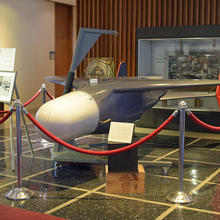 Photo of the restored Bat missile behind stanchions and ropes in the NIST library