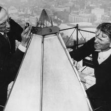 Two men sit on scaffolding and examine the tip of the Washington Monument.