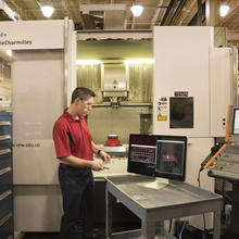 NIST researcher Tom Hedberg in a machine shop with computer monitor displaying CAD image