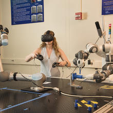 Researcher Megan Zimmerman wearing a virtual reality headset and handheld devices to control 2-handed tasks of a robot